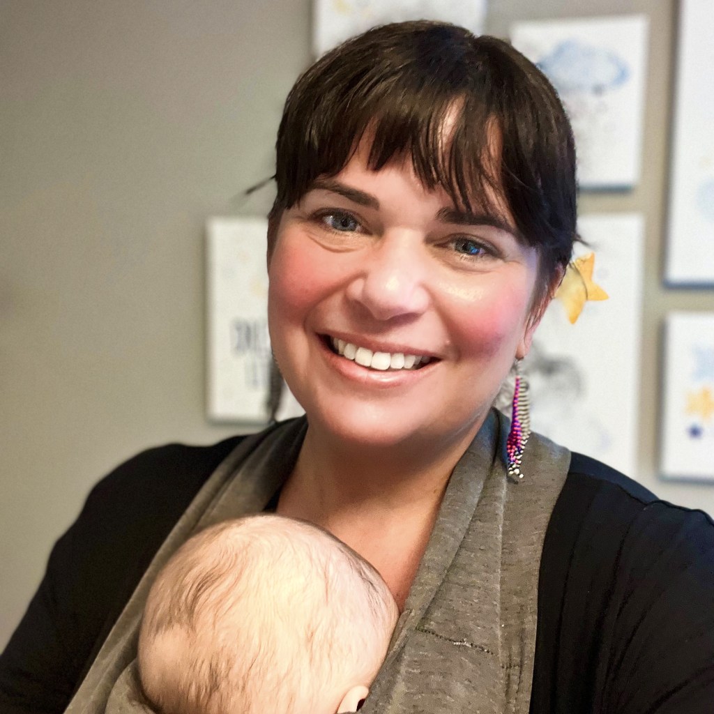 Photo of Sherilyn Saporito, smioing and wearing a baby in a babycarrier #doulainPittsburgh #PittsburghDoula #postpartumdoulaPittsburgh 